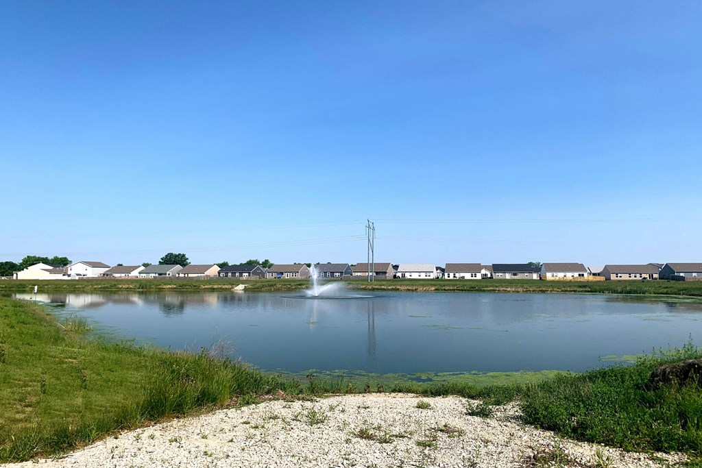 a pond with a fountain in the middle and houses in the background