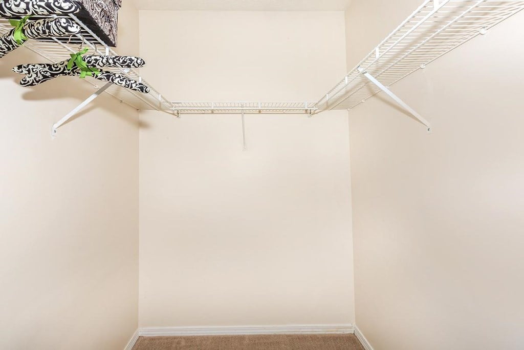 A white closet with a hanging shelf and clothes.