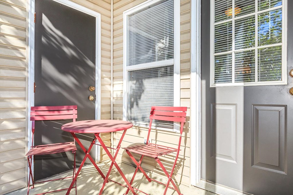 A red table and two chairs are on a porch.