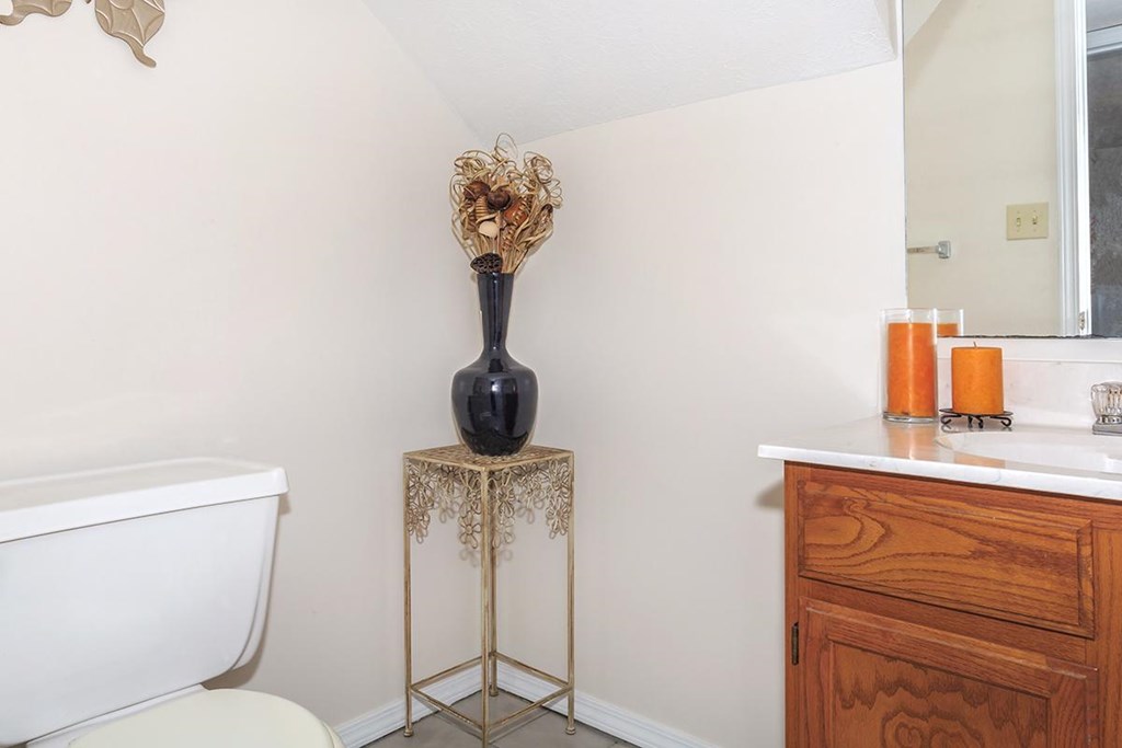 A bathroom with a white bathtub, a wooden vanity, and a vase on a stand.
