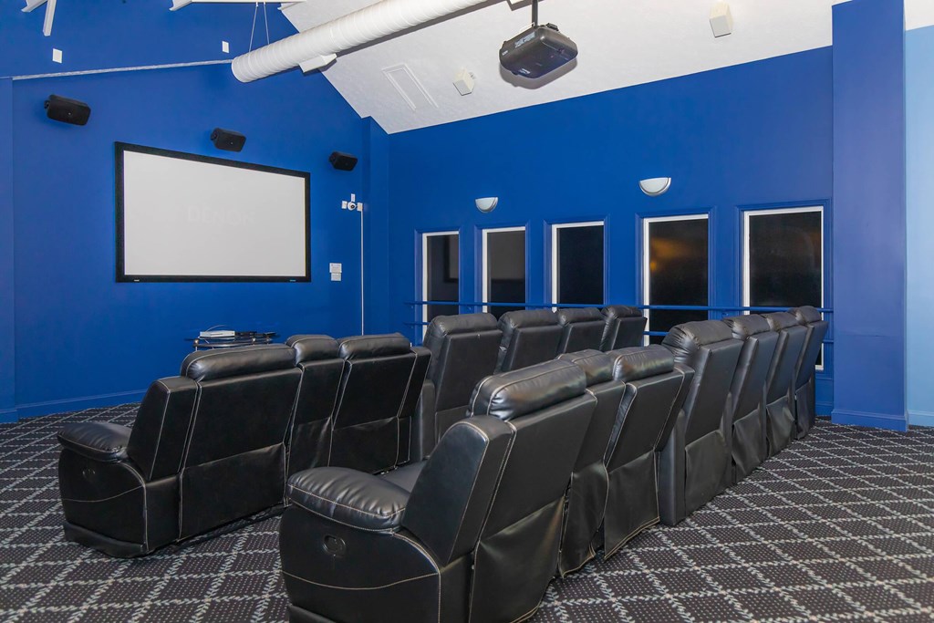 A row of black leather chairs are arranged in front of a white screen in a room with blue walls.