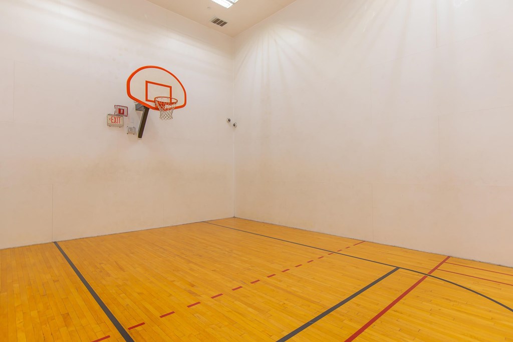 A basketball hoop is mounted on a wall in a room with a wooden floor.