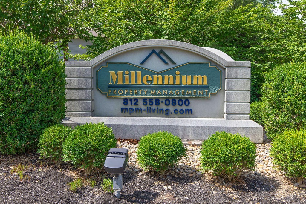 A sign for Millennium Property Management is displayed in front of some bushes.