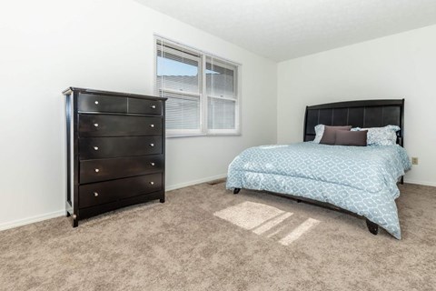 A bedroom with a black dresser and a blue bedspread.