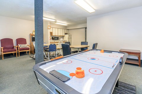 A shiny air hockey table is in the middle of a room with chairs and a kitchen in the background.