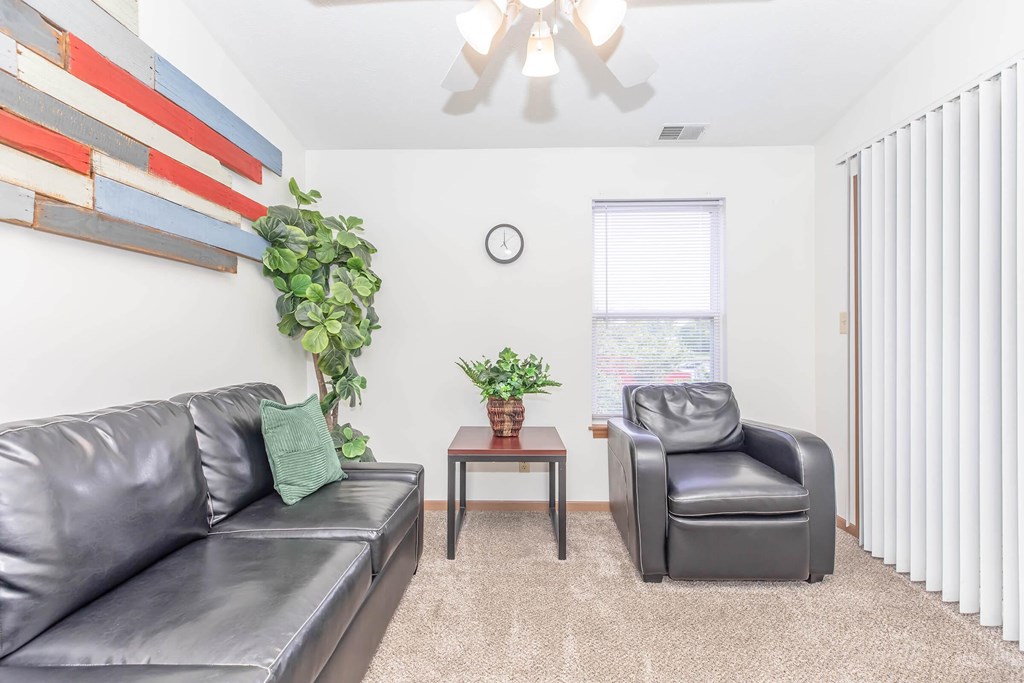 A living room with a grey couch, a black leather chair, and a wooden table with a plant on it.