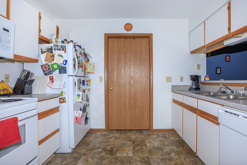 A kitchen with a refrigerator covered in magnets and a wooden door.