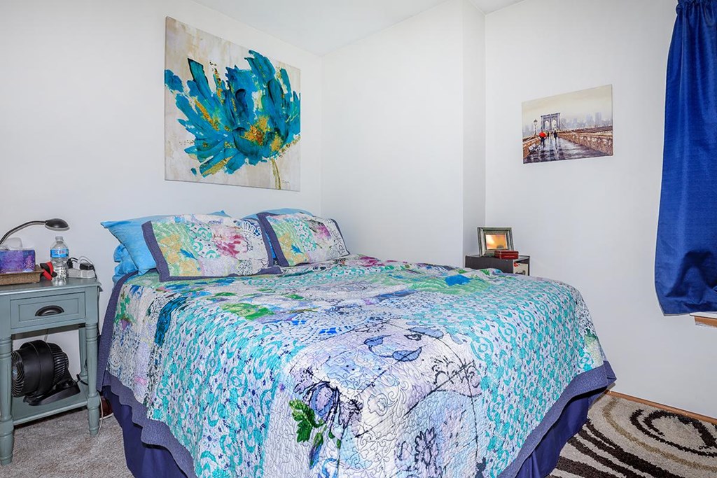 A bedroom with a bed covered in a blue and white floral comforter.