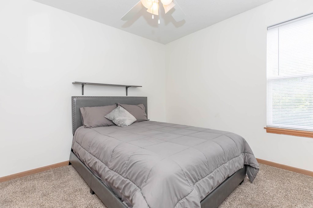 A bedroom with a bed, pillows, and a ceiling fan.