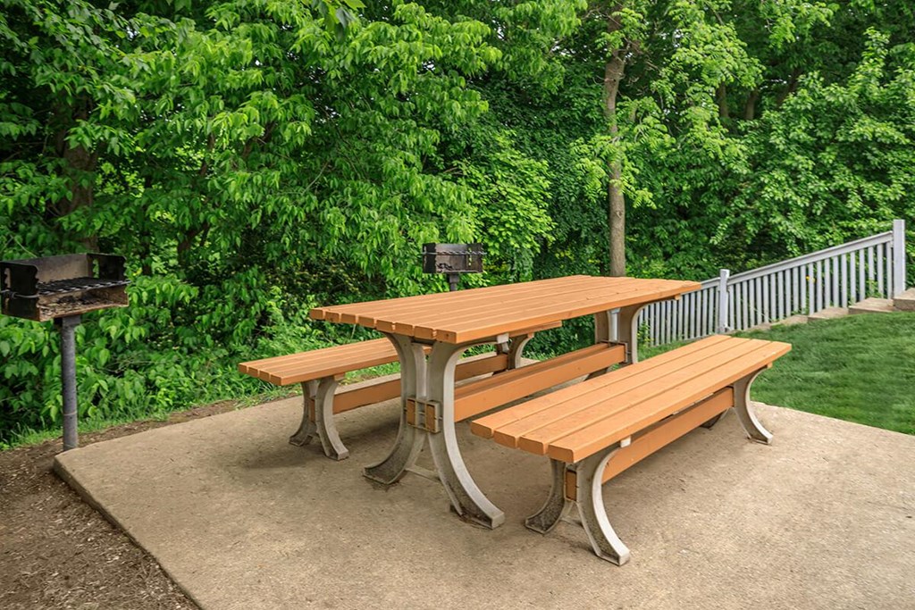 A wooden picnic table with two benches is set on a concrete surface.