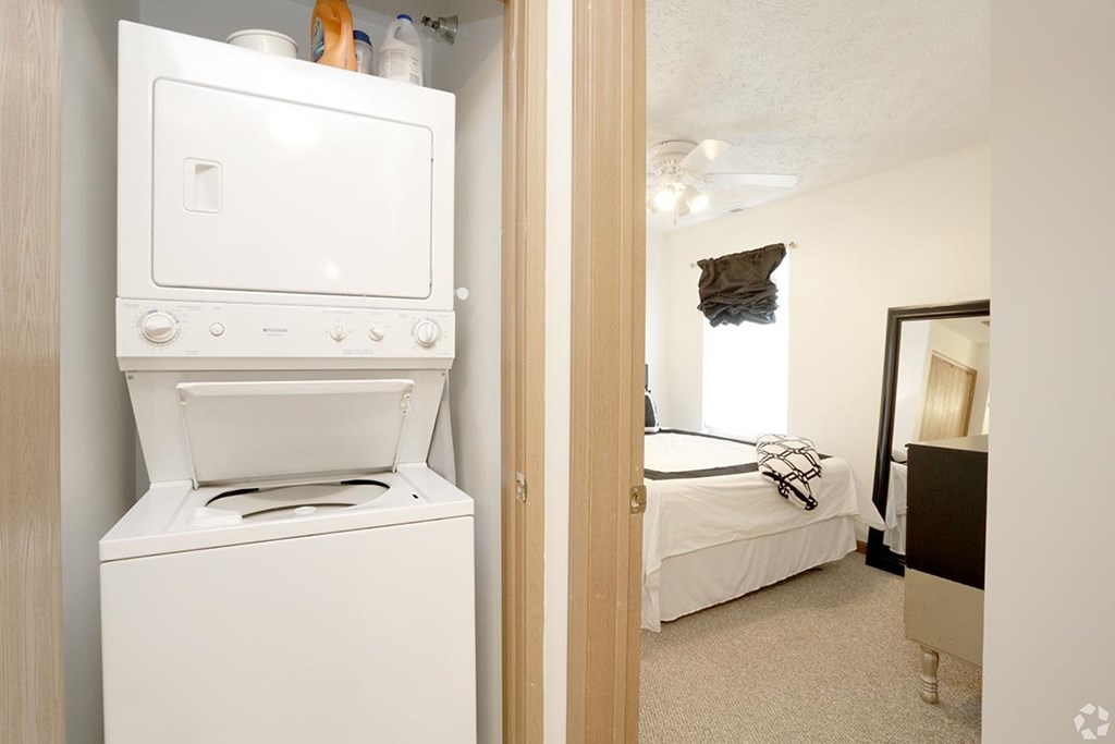A white oven and dryer are in a small room with a bed in the background.