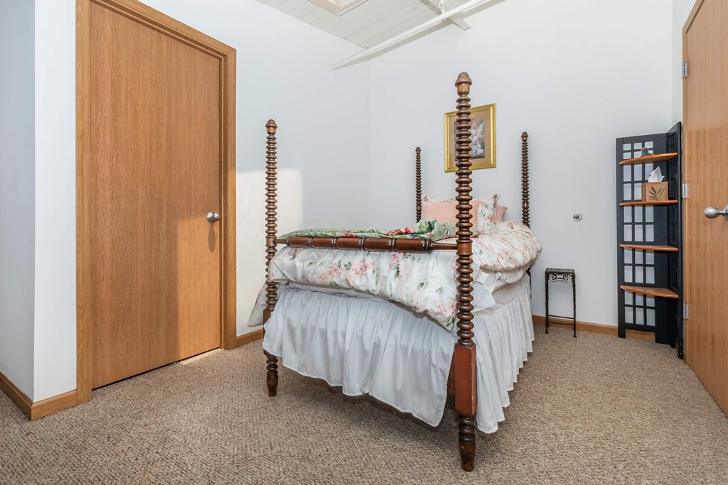 A bed with a wooden frame and four posts is in a room with a carpeted floor.