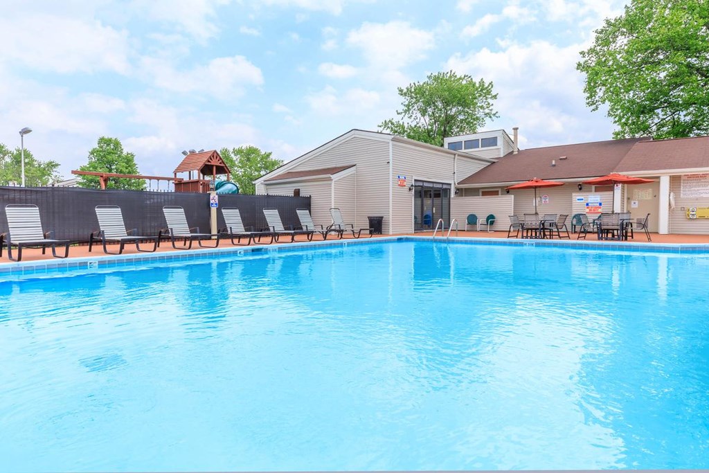 A large blue swimming pool with sun loungers and a building in the background.