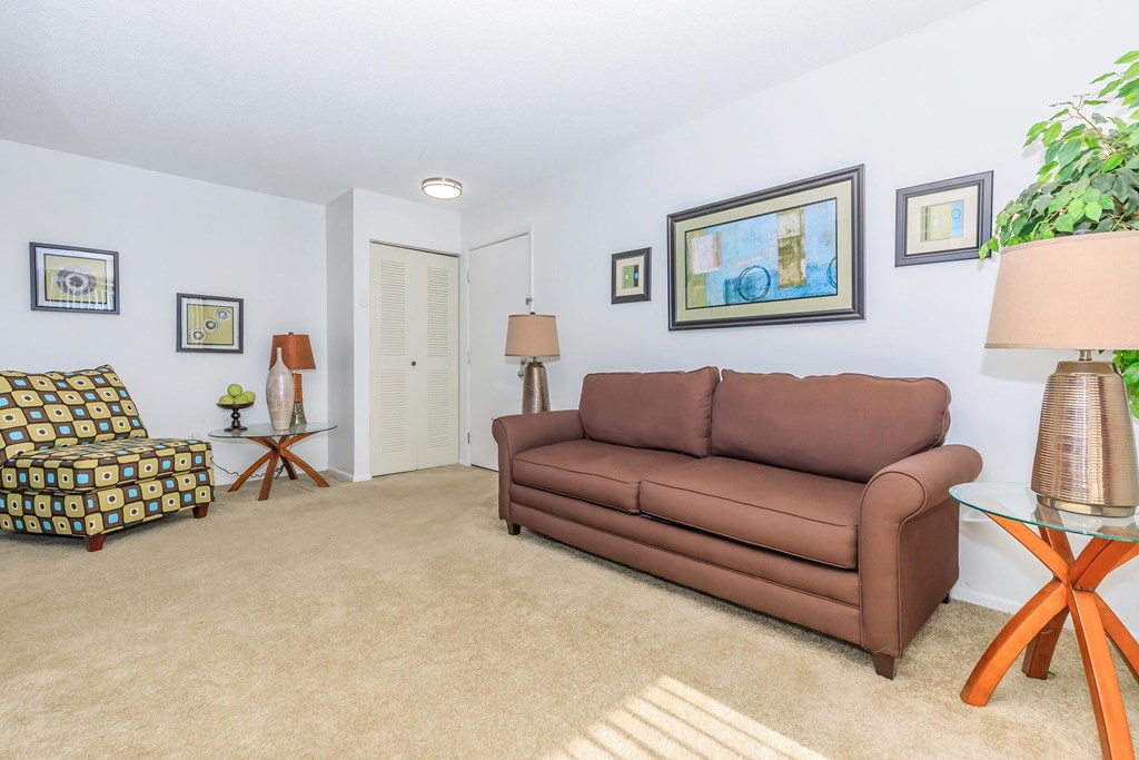 A living room with a brown couch, a patterned chair, and a glass coffee table.