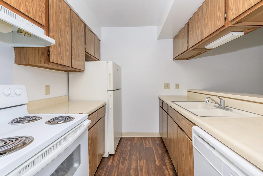 A kitchen with a white stove top oven and white refrigerator with wooden cabinets.