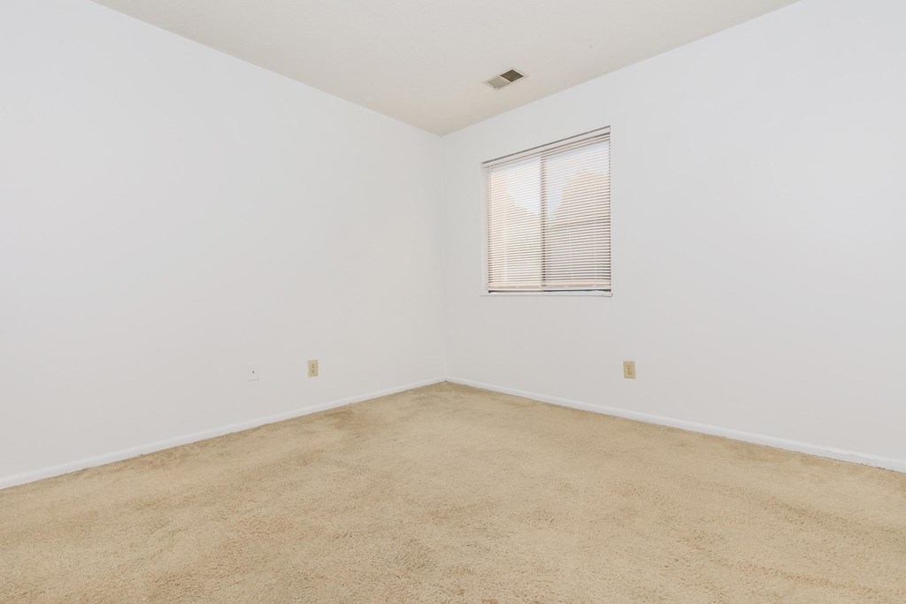 A room with a carpeted floor and a window with blinds.