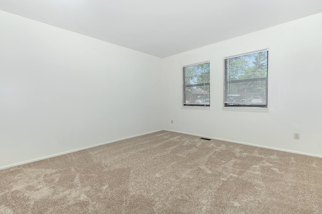 A room with a carpeted floor and two windows.