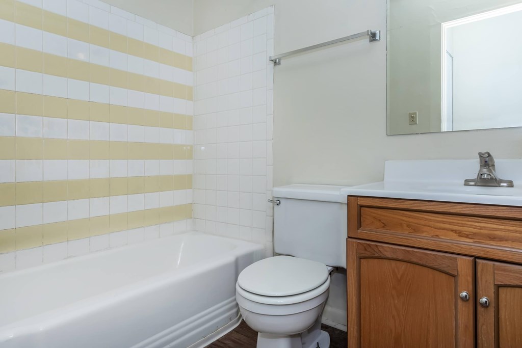 A white toilet sits next to a white bathtub in a bathroom with yellow and white tiles.