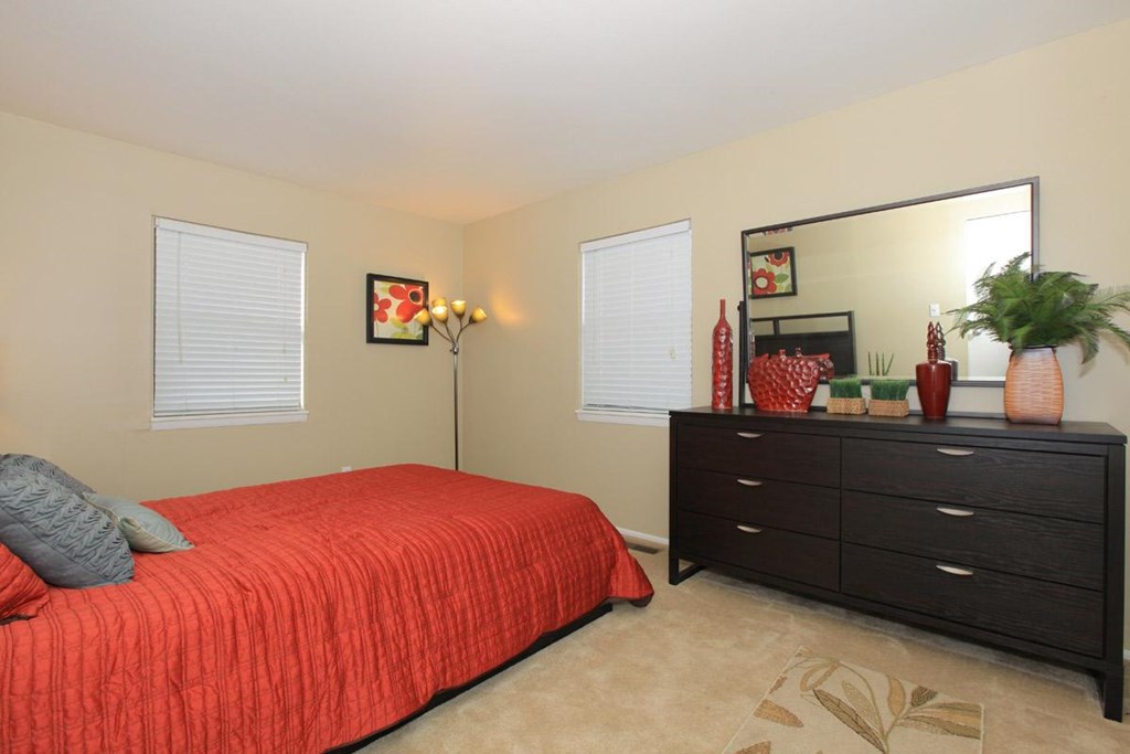 A bedroom with a red bedspread and a black dresser.
