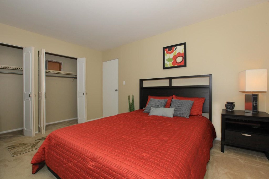 A bedroom with a red bedspread and a black headboard.