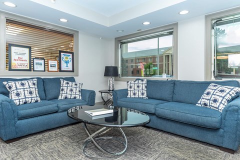 A living room with two blue couches and a glass coffee table.