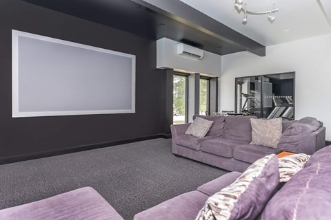 A living room with a grey couch and a large empty white screen on the wall.