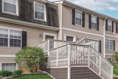 A two-story house with a deck and a tree in front.