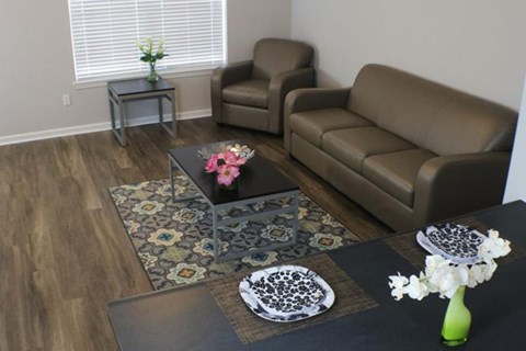 A living room with a brown couch, a glass table with flowers, and a rug.