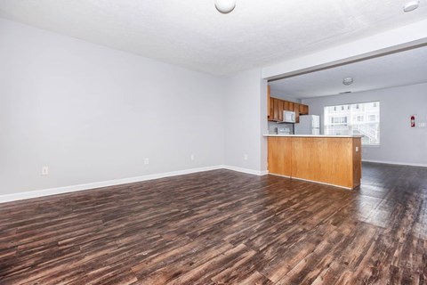 A room with wooden flooring and a kitchen area in the background.