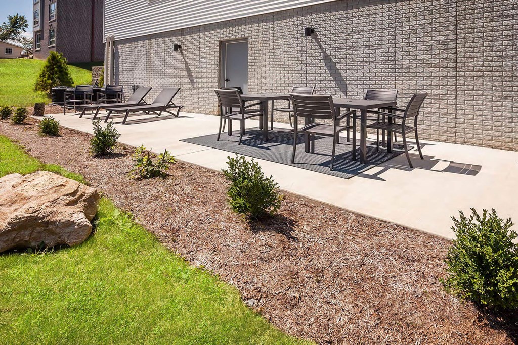 A patio with a table and chairs is surrounded by a gravel bed and a grassy area.