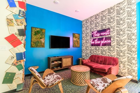 A living room with a red couch and a neon sign that says "This must be the place".