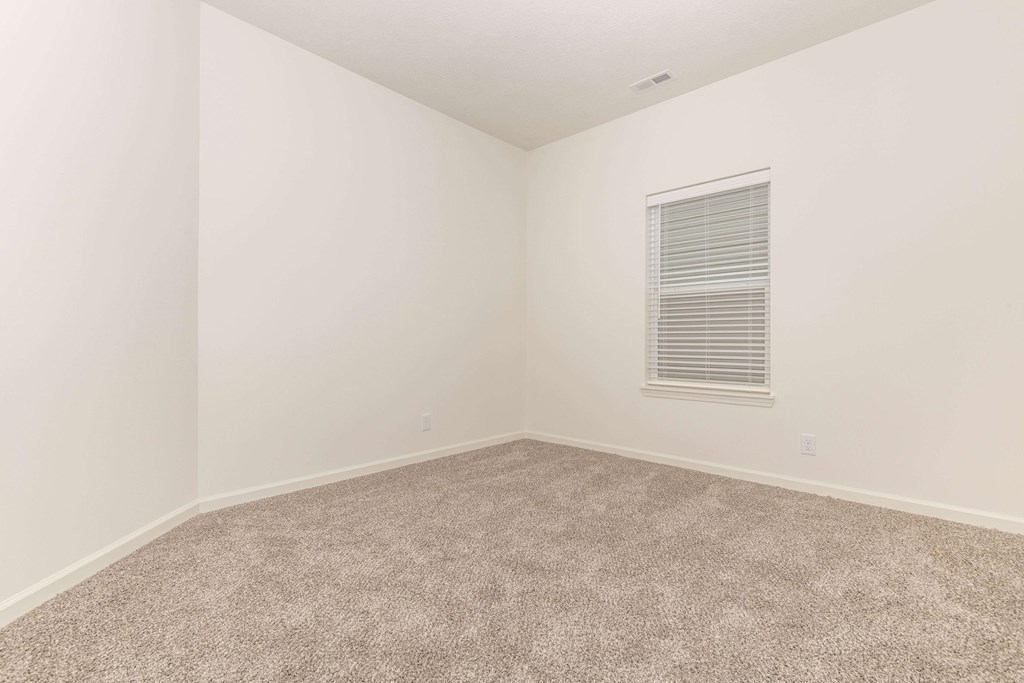 A room with a carpeted floor and a window with blinds.