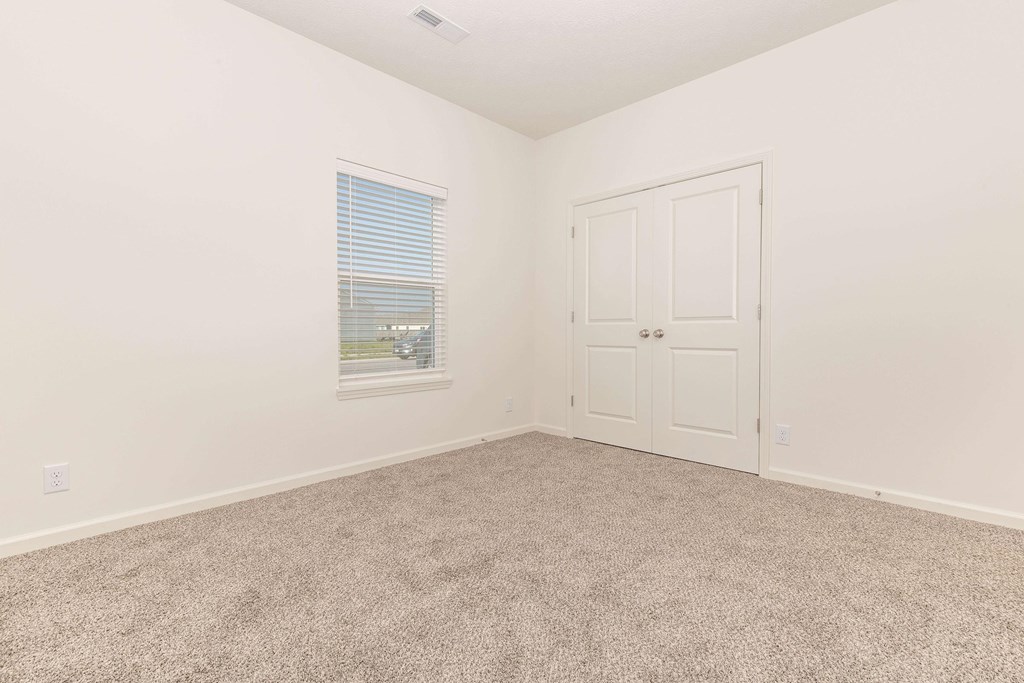 A room with a carpeted floor, a window with blinds, and a white door.