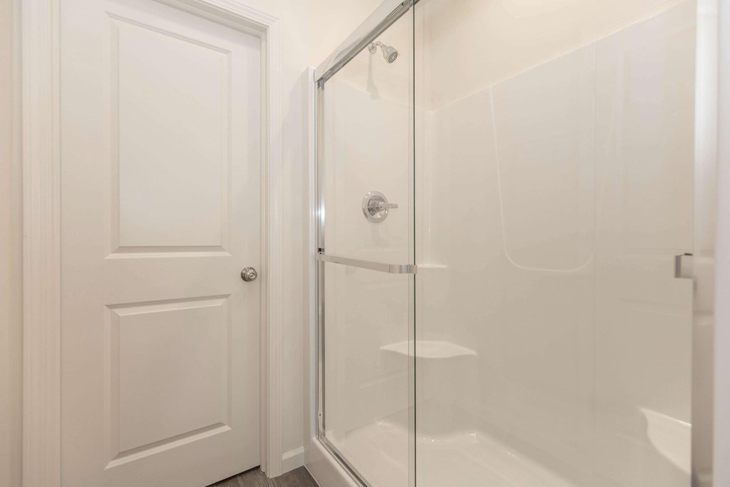 A white door is open to a glass shower stall.