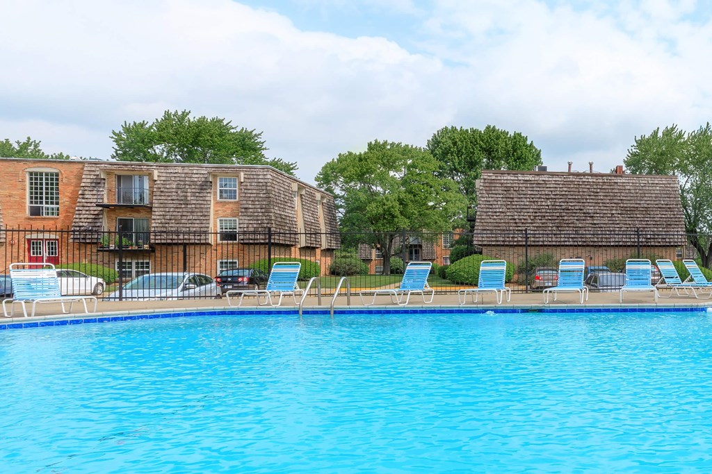 A swimming pool in front of a building with lounge chairs.