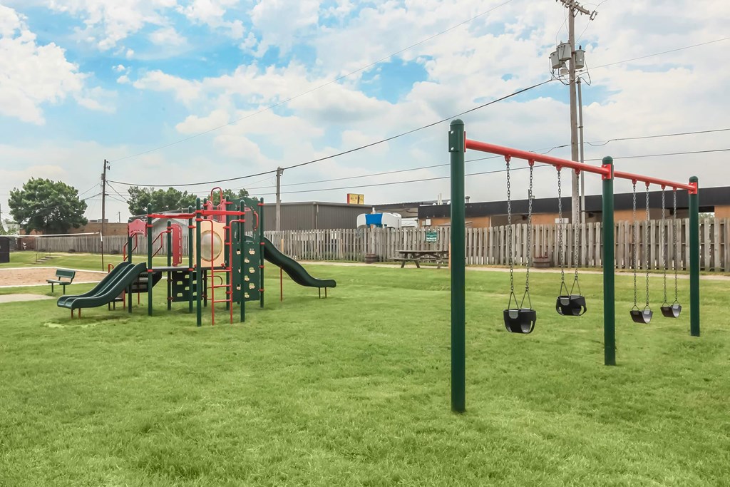 A playground with a red swing set and a green slide.