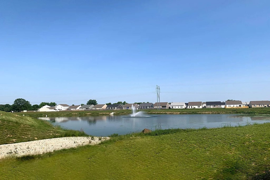 A body of water surrounded by grass and houses in the distance.