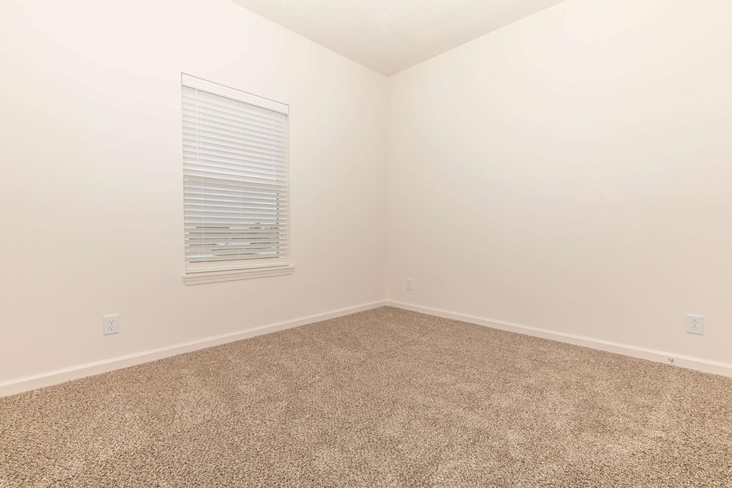 A room with a carpeted floor and a window with blinds.