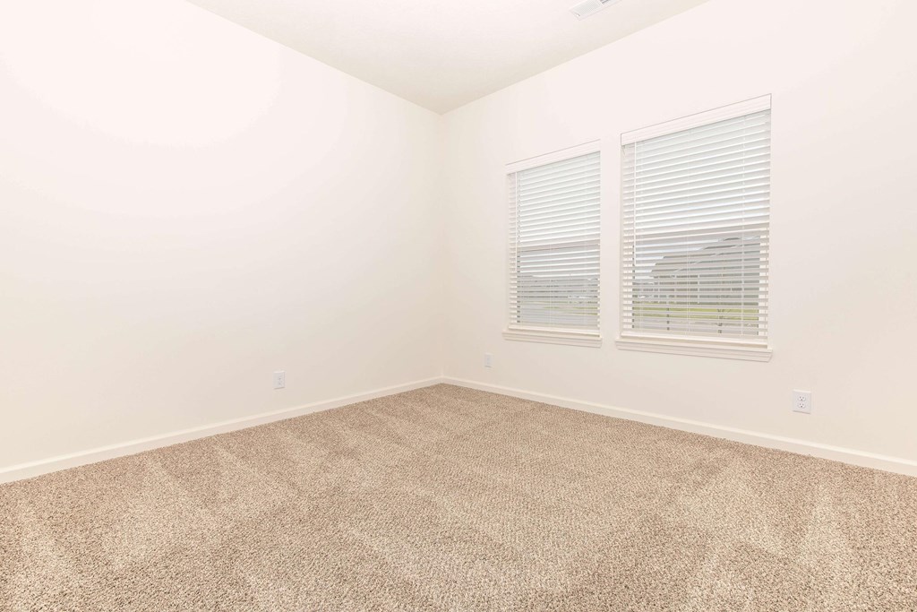 A room with carpeted floor and two windows.