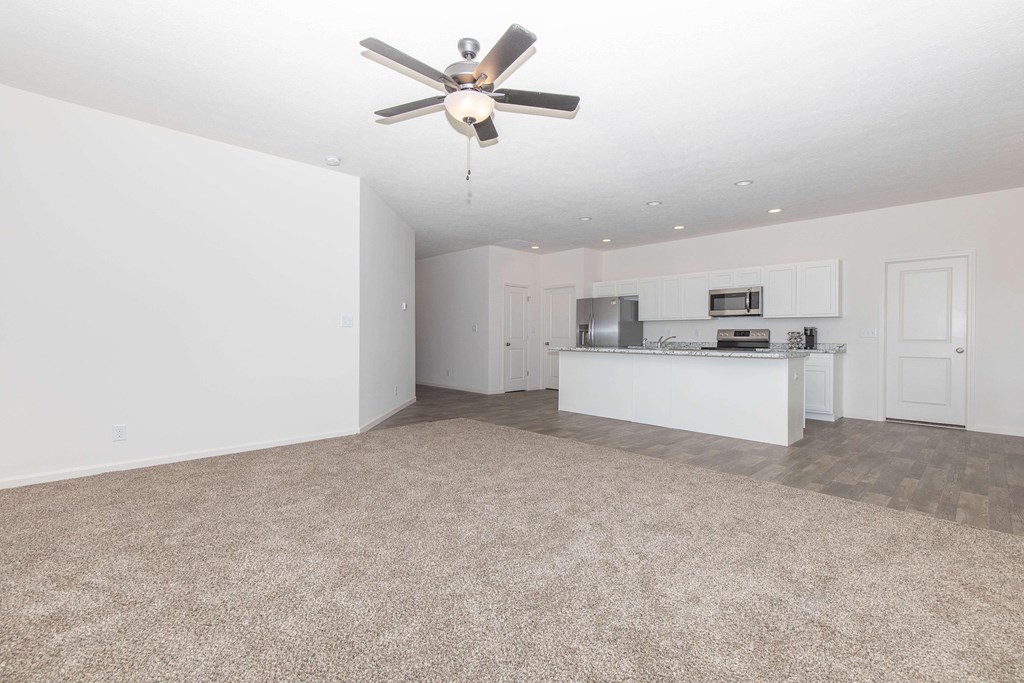 A room with a ceiling fan and a kitchenette.