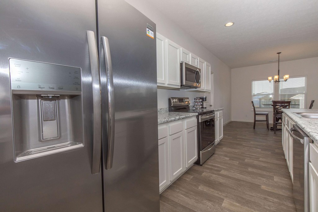 A modern kitchen with a stainless steel refrigerator and wooden flooring.