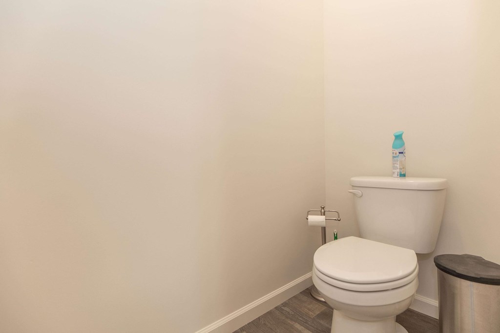 A white toilet with a roll of toilet paper on the wall.