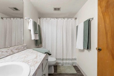 A white bathroom with a marble sink and a shower curtain.