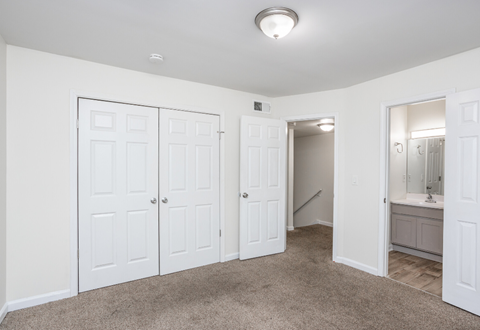 a bedroom with three closets and a bathroom with a sink and a mirror