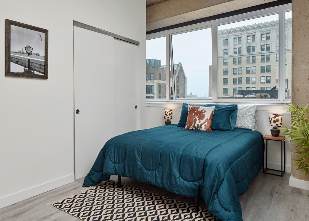 A bedroom with a blue bedspread and a black and white patterned rug.