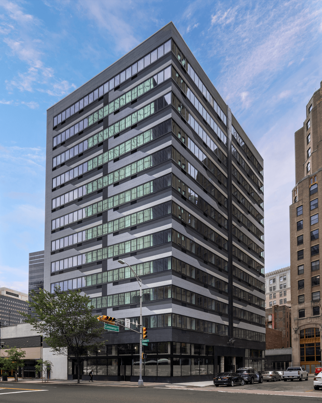 A modern multi-story building with a glass facade is situated on a street corner.