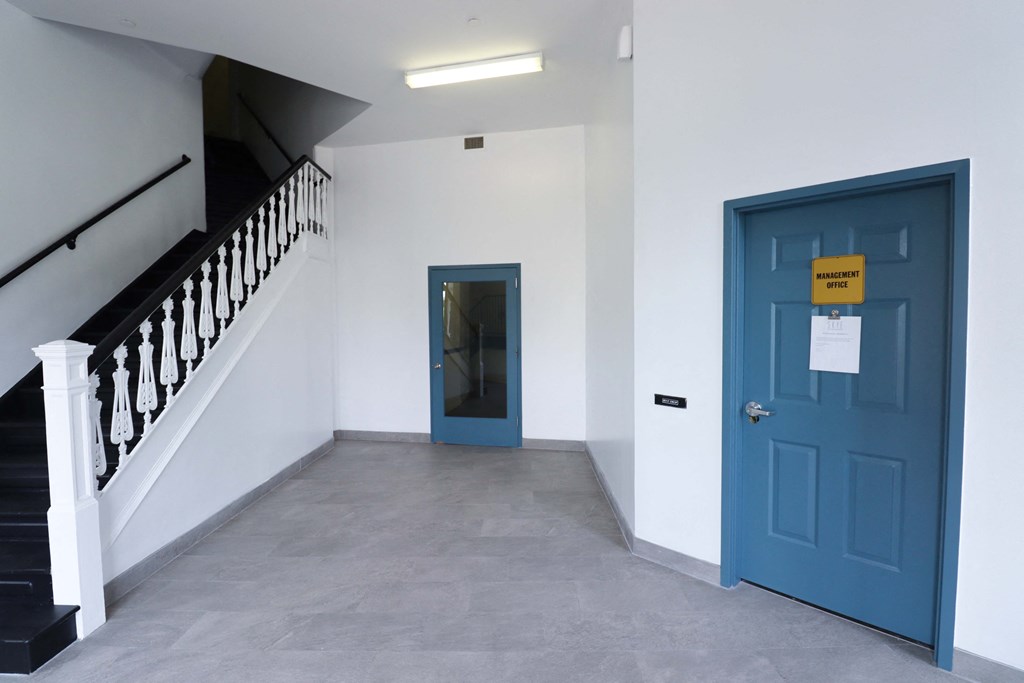a blue door in a white walled room with a staircase in the background