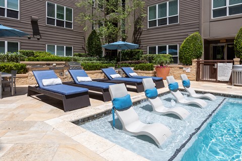 A pool with a blue umbrella and lounge chairs.
