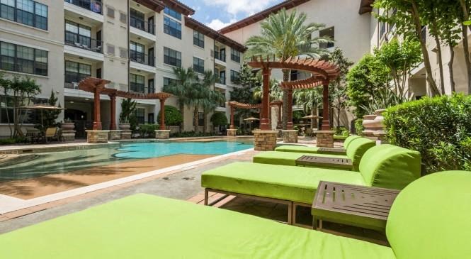 a large swimming pool with green lounge chairs in front of a building