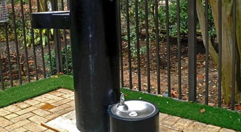 a stainless steel water fountain in front of a black fence